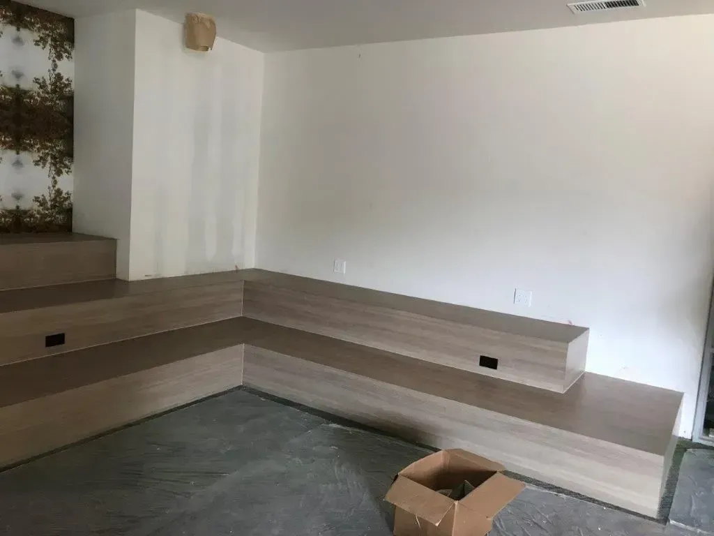 Built-in wooden seating unit in a room with white walls and a patterned wall section.