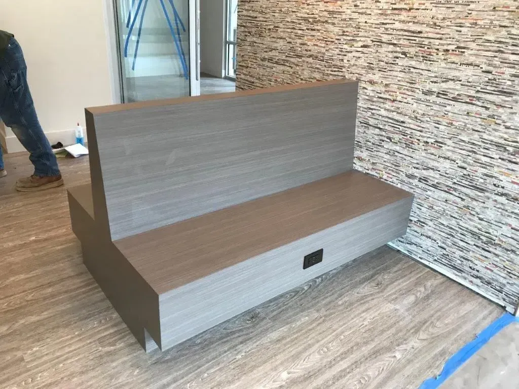 Gray wooden bench with a built-in power outlet, against a stone wall in a room.