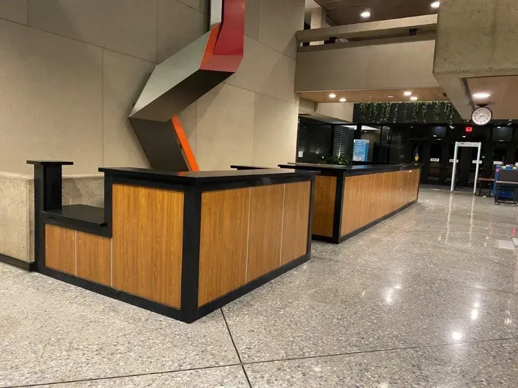Two wooden reception desks with black trim in a building lobby. A geometric art piece is on the wall.