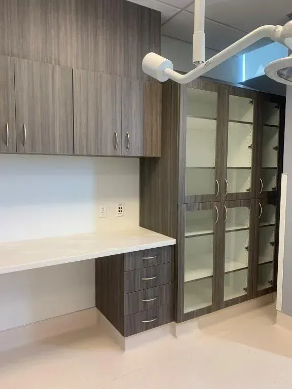 A medical room with gray cabinets, a white desk, and glass-door storage.