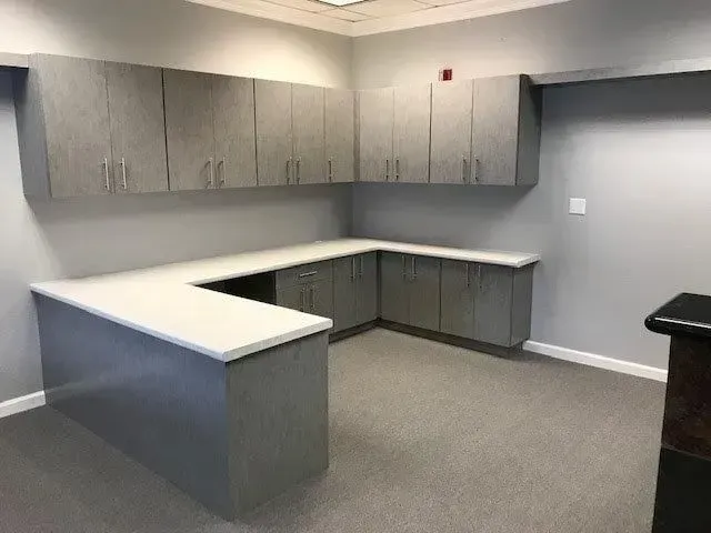 Gray office cabinets with white countertops against gray walls, on gray carpet.