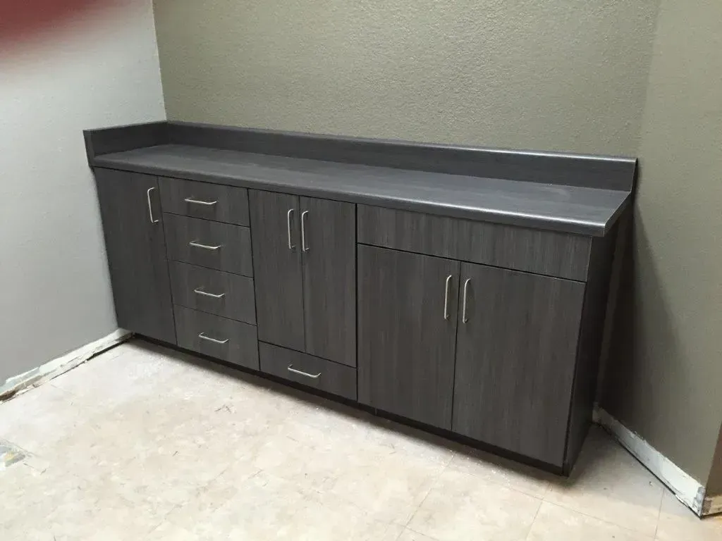 Gray cabinet unit with doors and drawers against a gray wall and white trim.