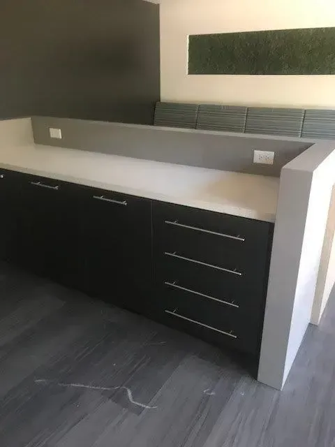 Black and white office counter with outlets on top, drawers, and white surface. Dark gray wall behind.