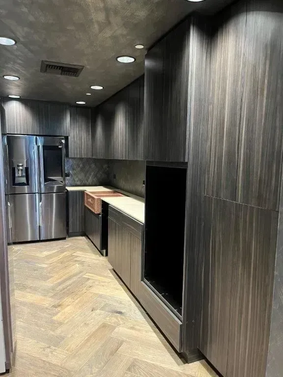 Modern kitchen with dark wood cabinets, stainless steel appliances, and herringbone floors.