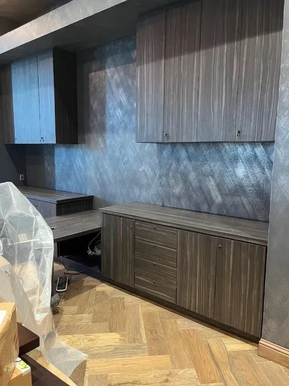 Built-in office cabinetry with upper and lower storage, desk, and drawer against a textured gray wall; wooden floor.