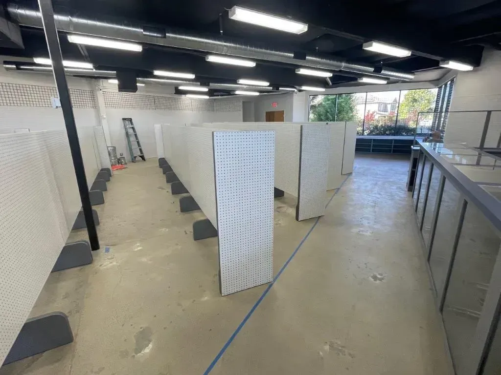 Empty retail space under construction with pegboard walls and fluorescent lighting.