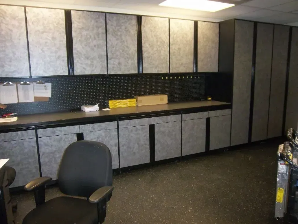 Gray and black workshop cabinets and workspace, with a black chair and floor.