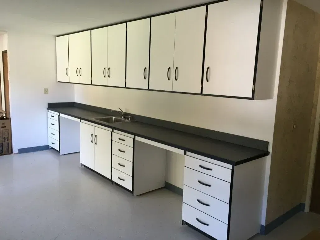 White cabinets with black trim above a gray countertop with a sink and cabinets below.