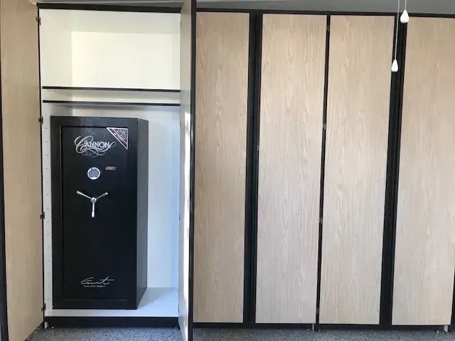 Built-in closet with a black safe inside. Light wood closet doors with black trim.