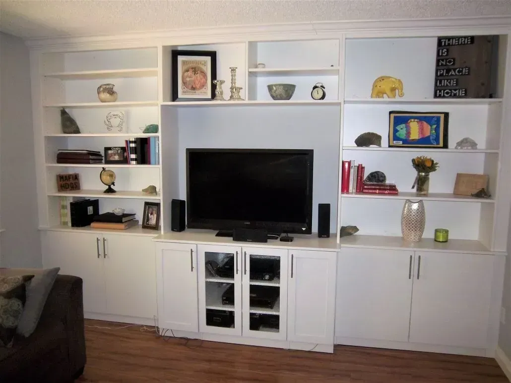 White built-in entertainment center with shelves, cabinets, and a television on a wood floor.