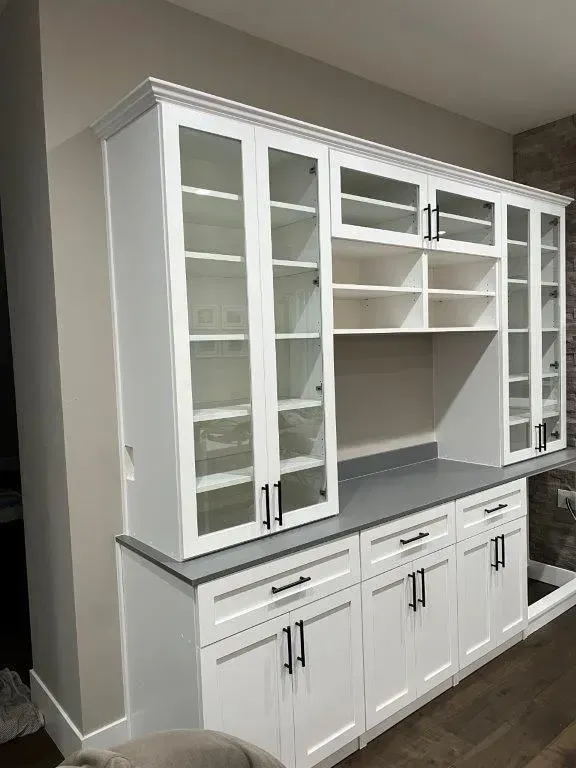 White kitchen cabinets with glass doors, black hardware, and gray countertop.
