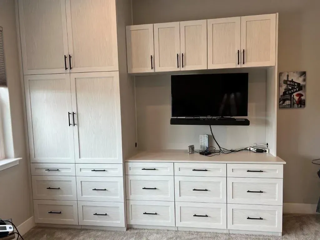 White built-in cabinetry with drawers and doors, a TV, and shelves in a room.