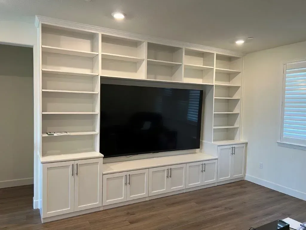 White built-in entertainment center with shelving, cabinets, and a large black TV.