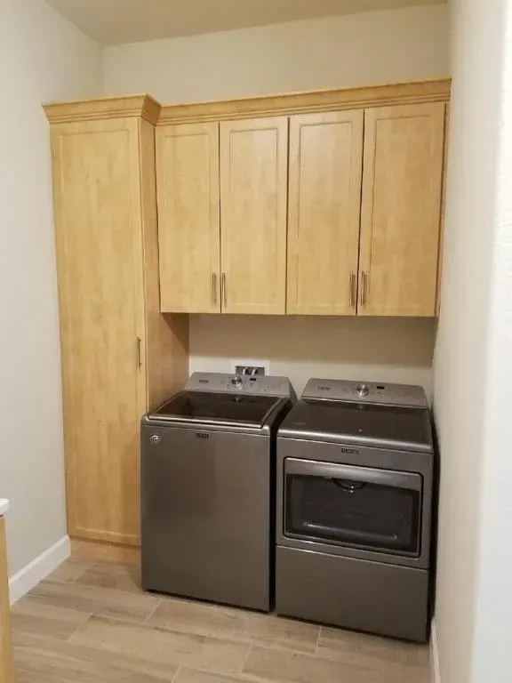 Laundry room with wood cabinets, silver washer and dryer, and tile flooring.