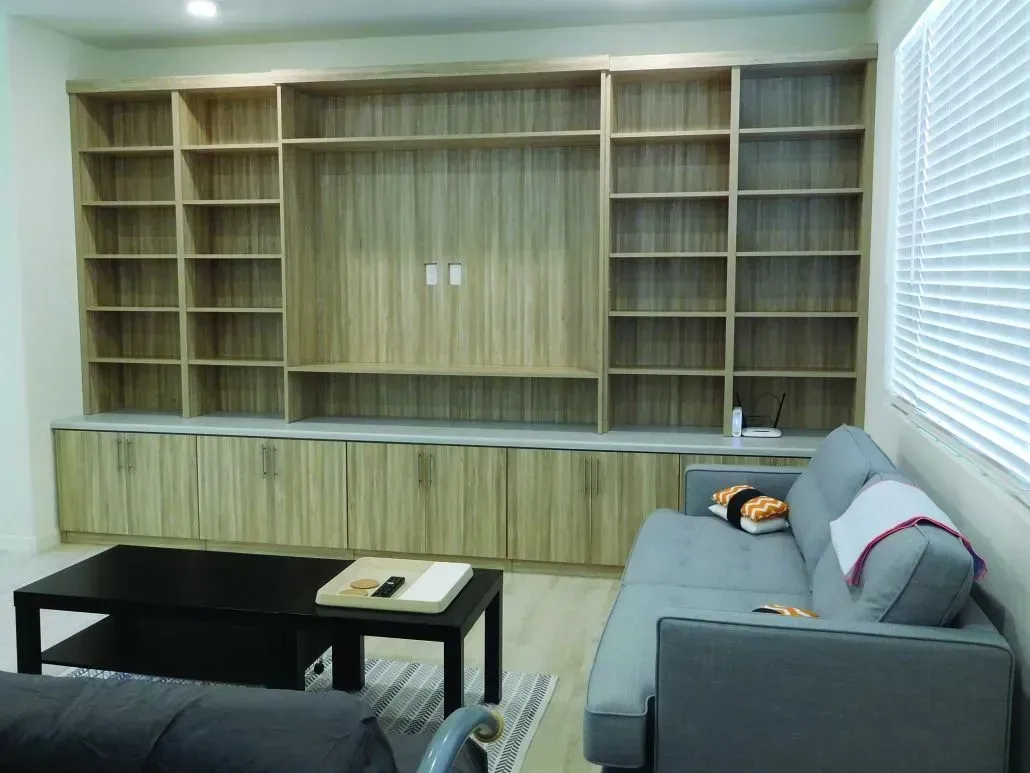 Wooden built-in shelving and cabinets in a living room, with a black coffee table and gray couch.