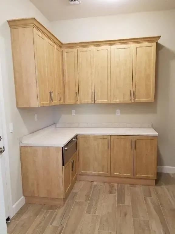 Light wood cabinets in a corner laundry room, with a white countertop and tile floor.