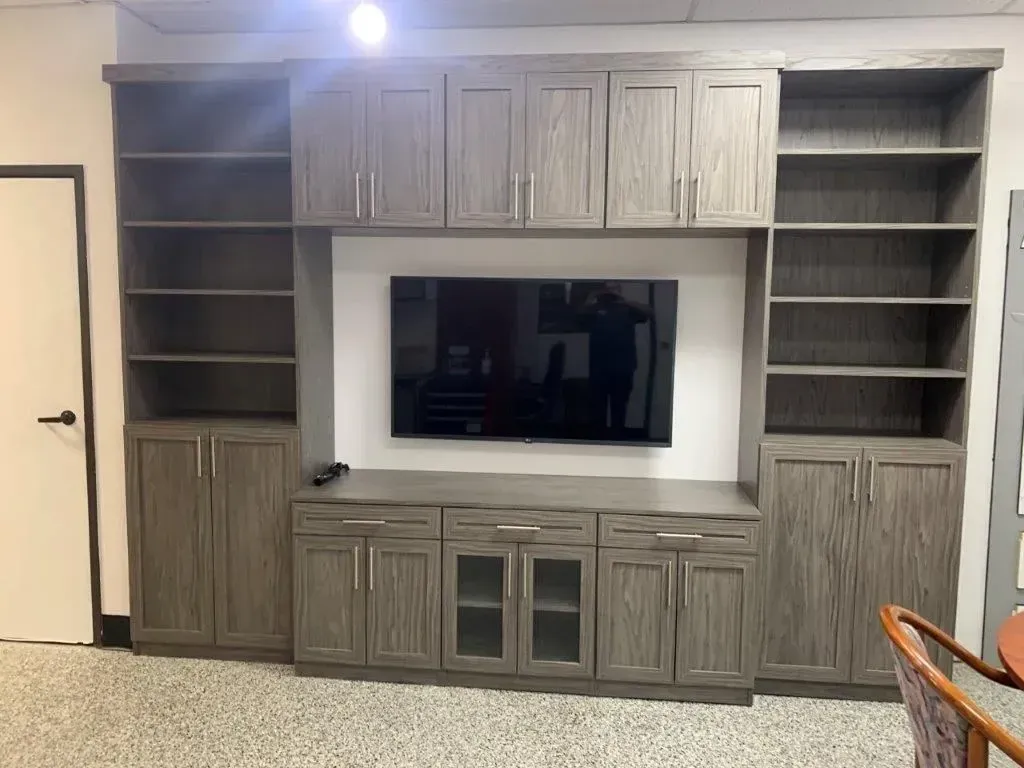 Built-in gray entertainment center with cabinets, shelves, and a mounted TV.