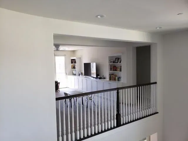 A two-story interior with a railing overlooking a kitchen and dining area. White walls and black accents.