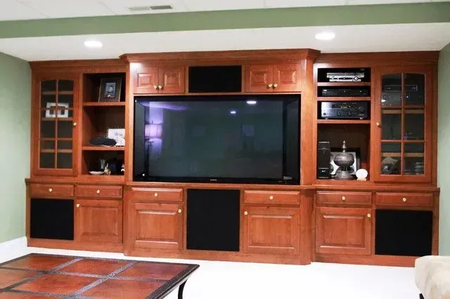 Built-in wooden entertainment center with TV, speakers, and storage cabinets in a room.