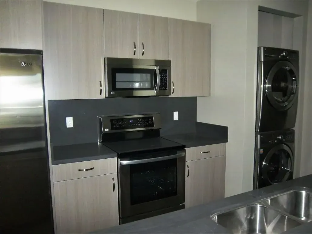Kitchen with stainless steel appliances, light wood cabinets, and dark countertop. Stacked washer/dryer on right.
