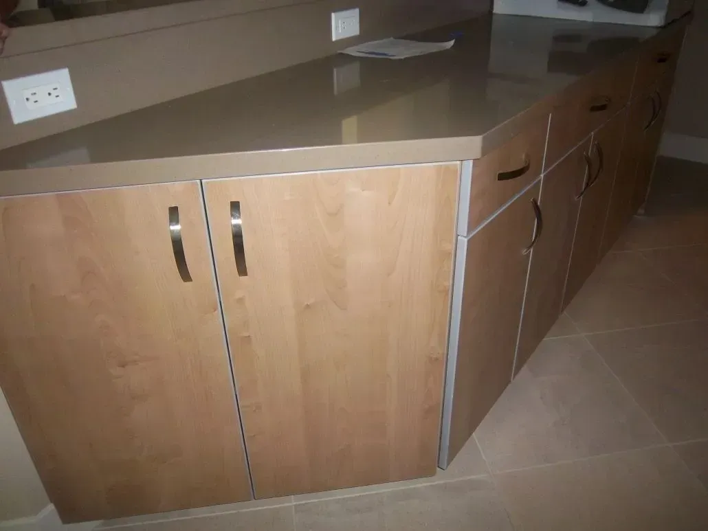 Kitchen island with light wood cabinets, dark countertop, and silver hardware.