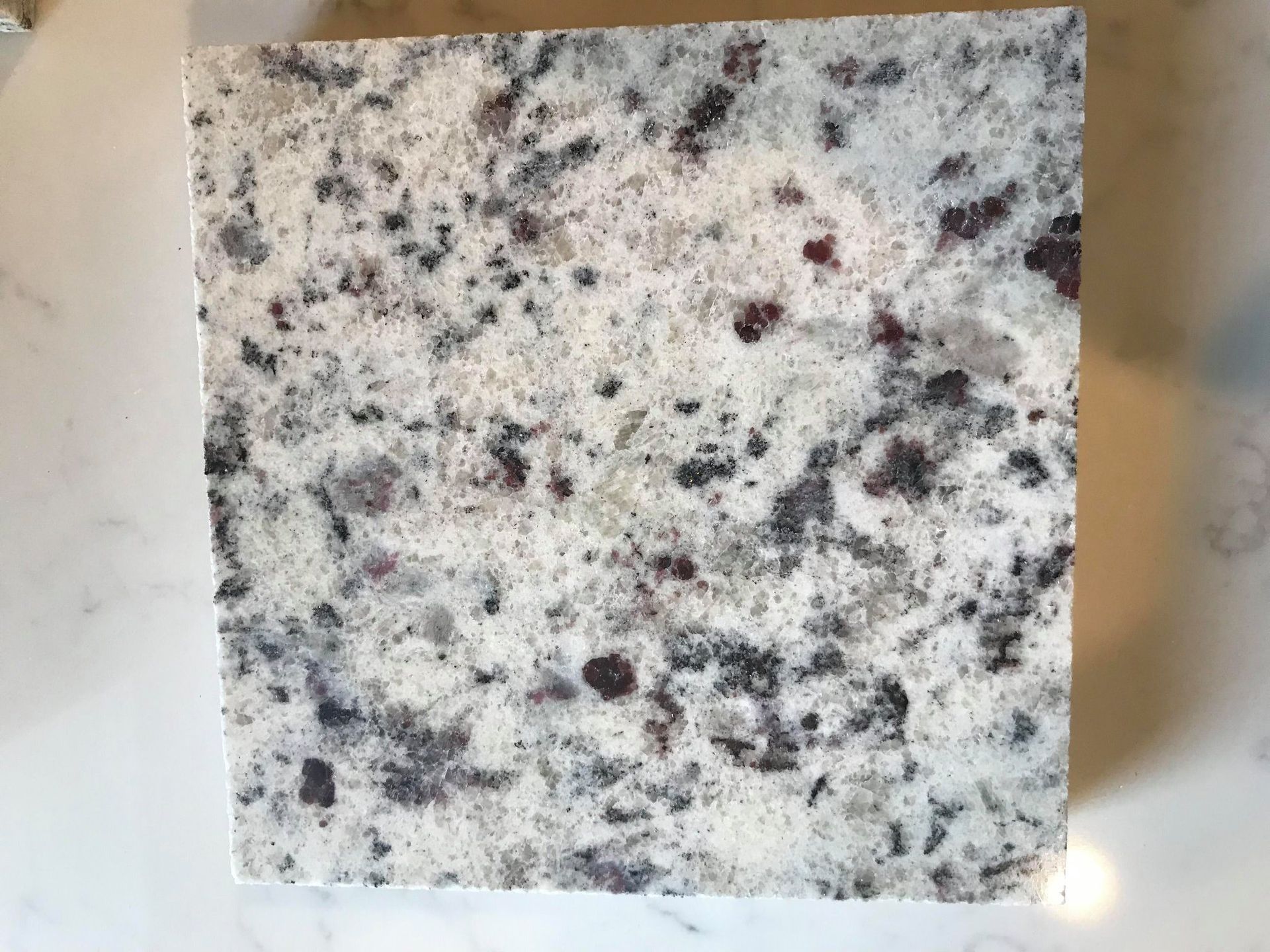 A square piece of granite is sitting on a white surface.