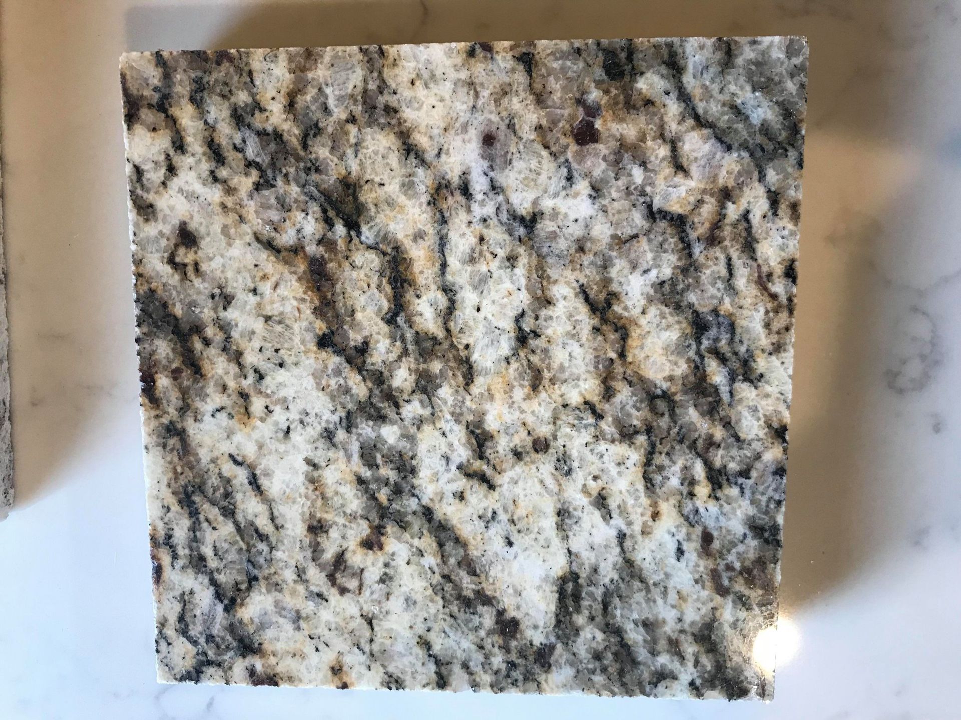 A square piece of granite is sitting on a white surface.