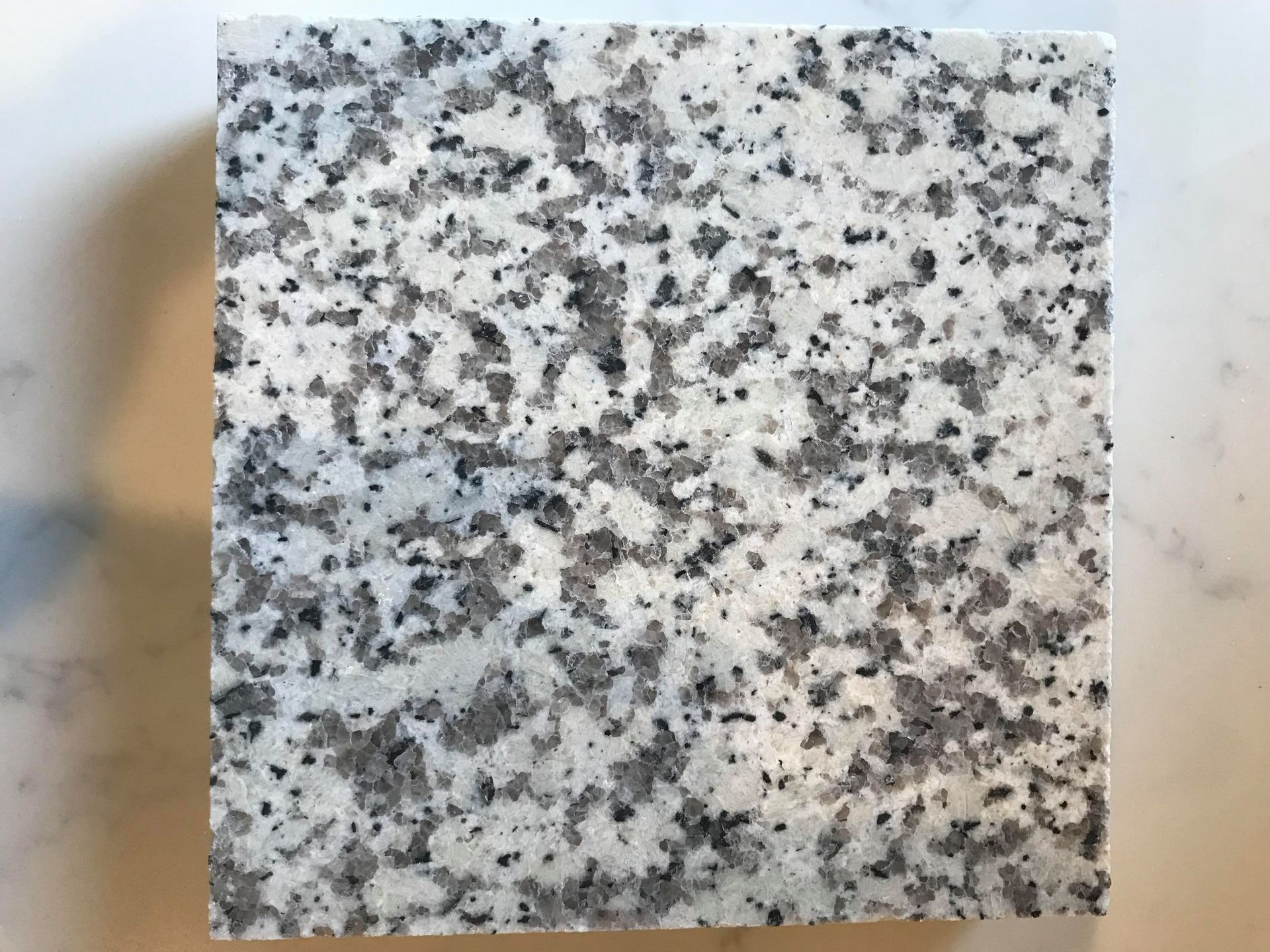 A square piece of granite with black and white spots on a white surface.