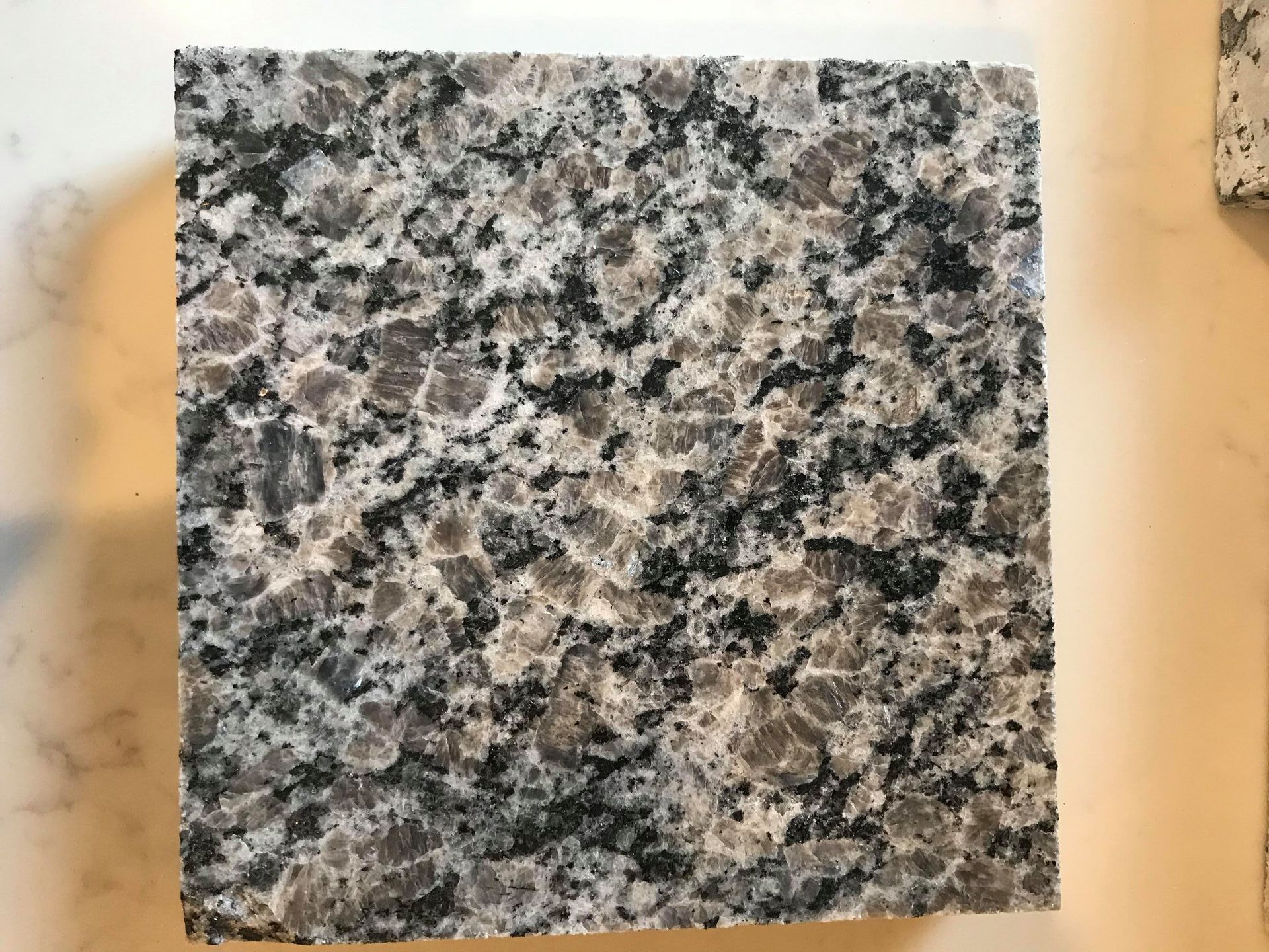 A square piece of granite is sitting on a white surface.