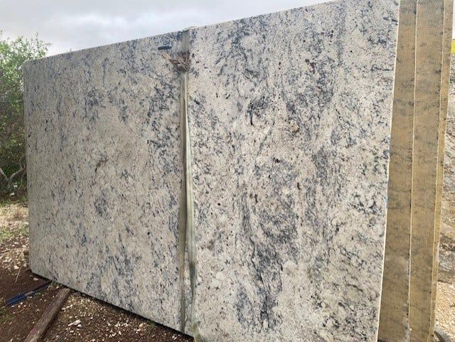A large white granite slab is sitting on top of a dirt field.