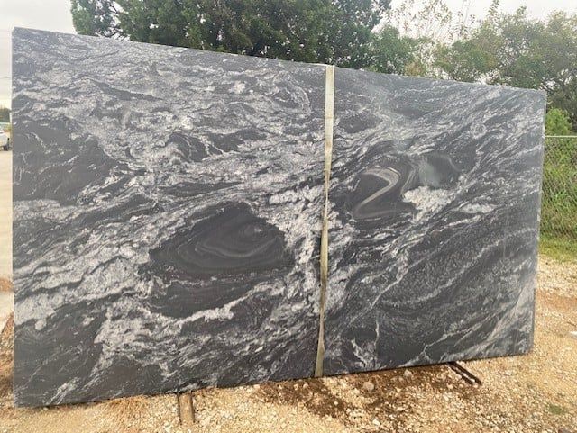 A large black granite slab is sitting on top of a dirt field.