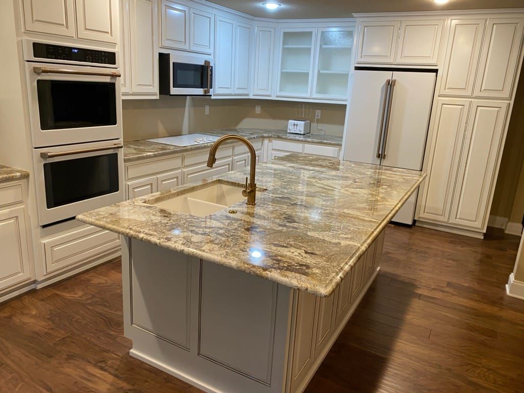 A kitchen with white cabinets , granite counter tops , a sink , and a refrigerator.