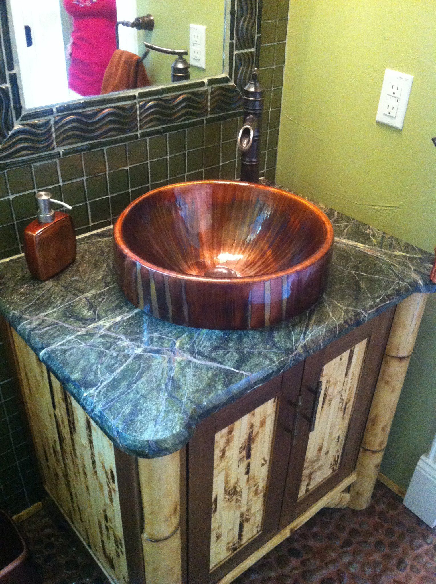 A bathroom vanity with a copper sink and a mirror.