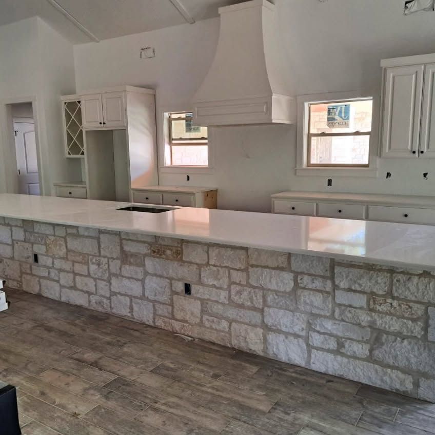 A kitchen with a brick wall and white cabinets and counter tops.