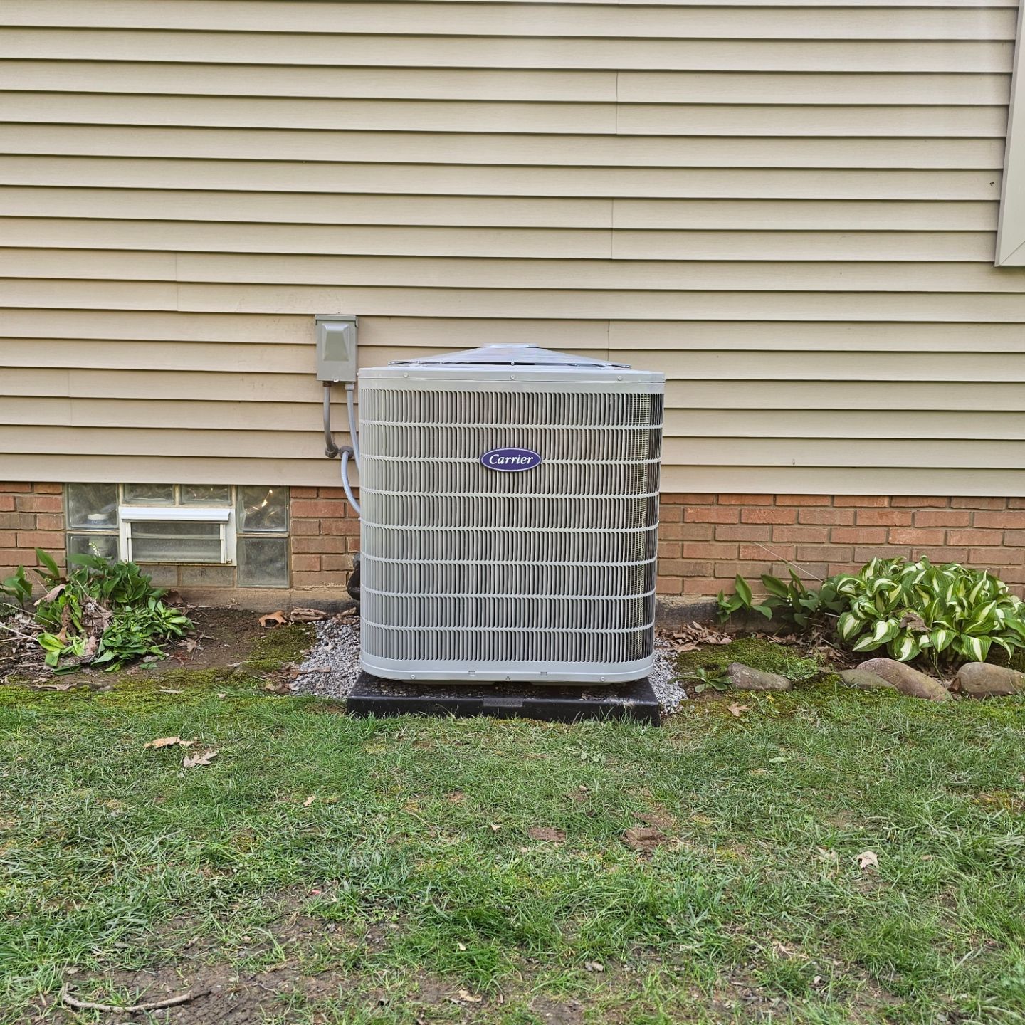 A large air conditioner is sitting in the grass in front of a house.