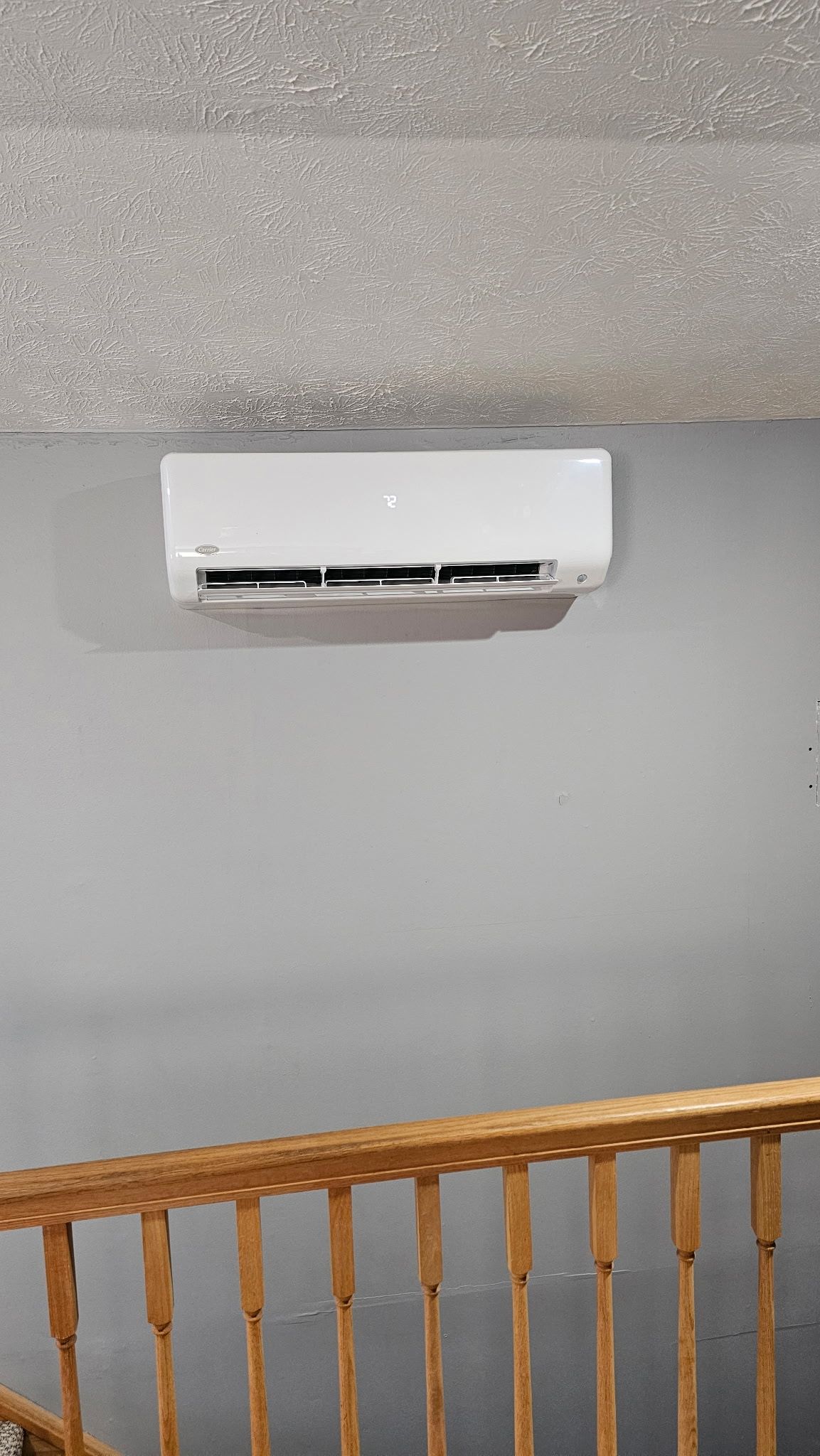 A white air conditioner is mounted on a wall next to a wooden railing.