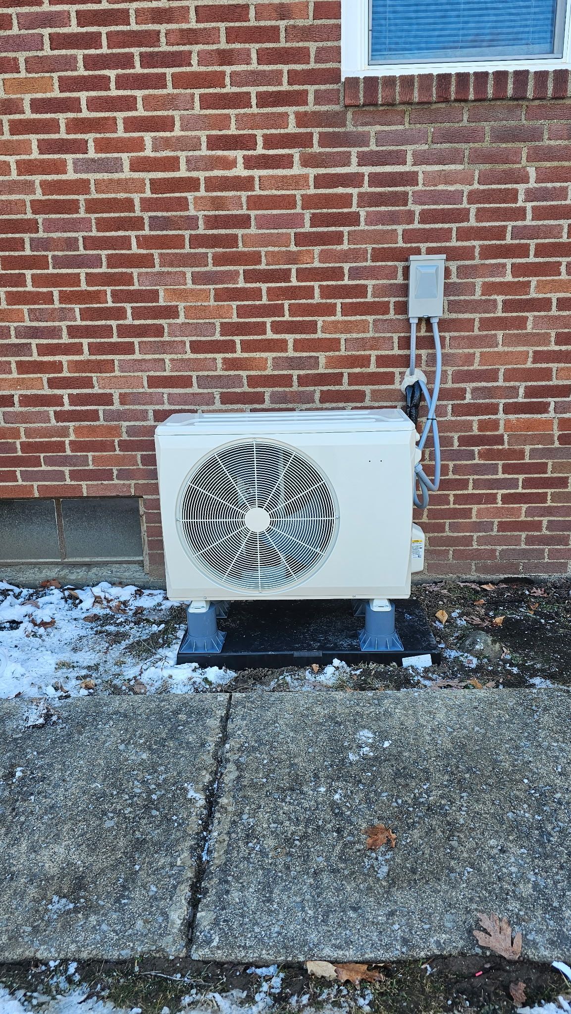 A white air conditioner is sitting on the sidewalk in front of a brick building.