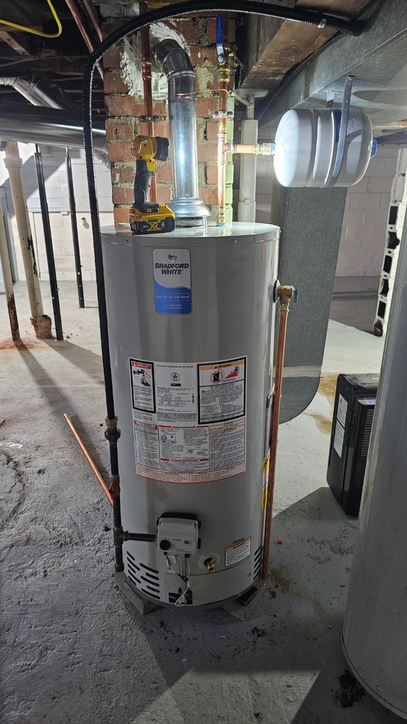 A water heater is sitting in a basement next to a brick wall.