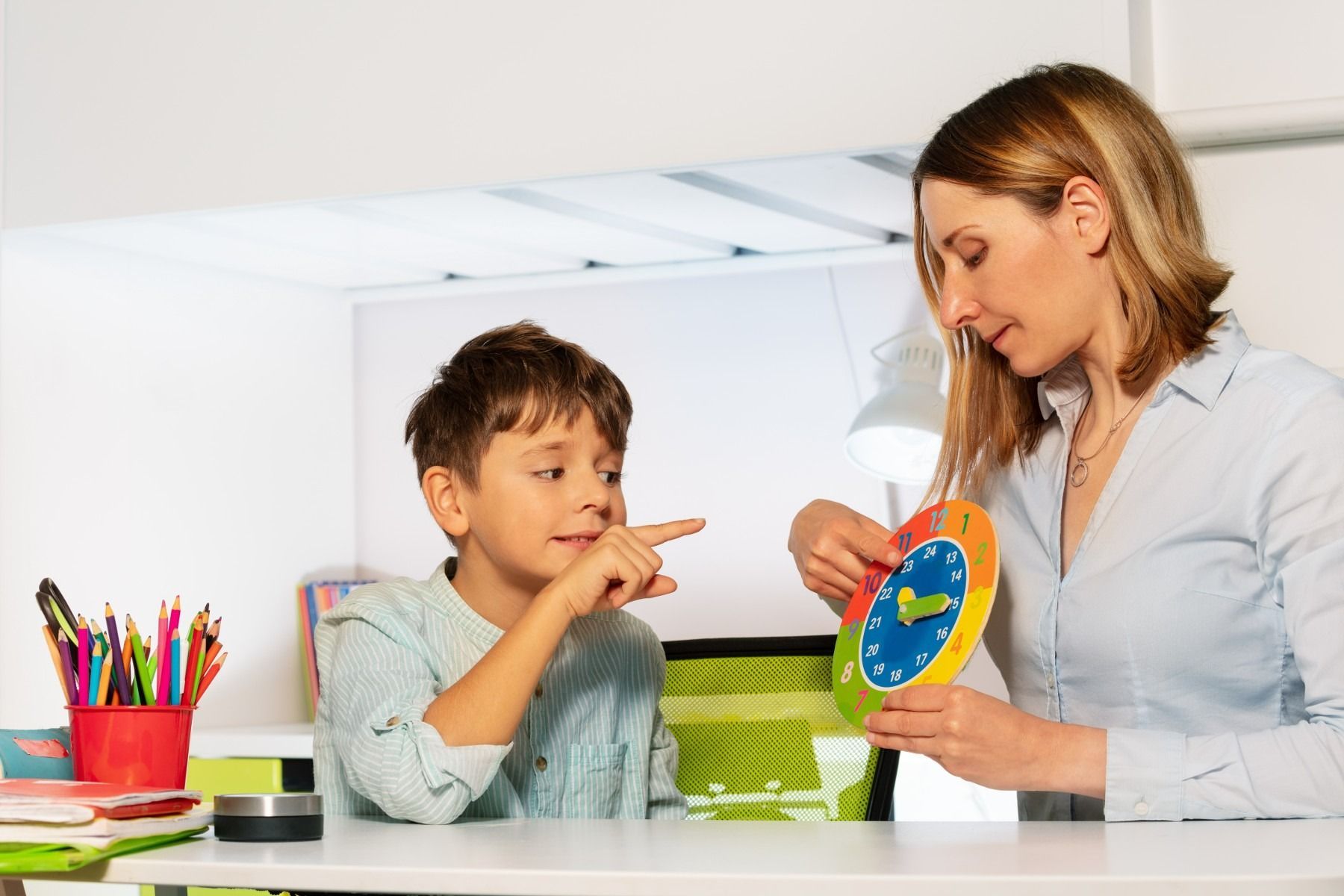 A woman is teaching a young boy how to read a clock.