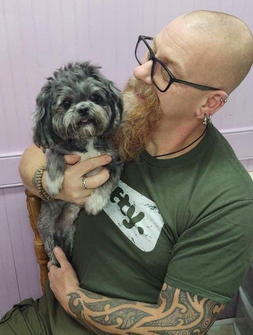 A man with a beard is holding a small dog in his arms.
