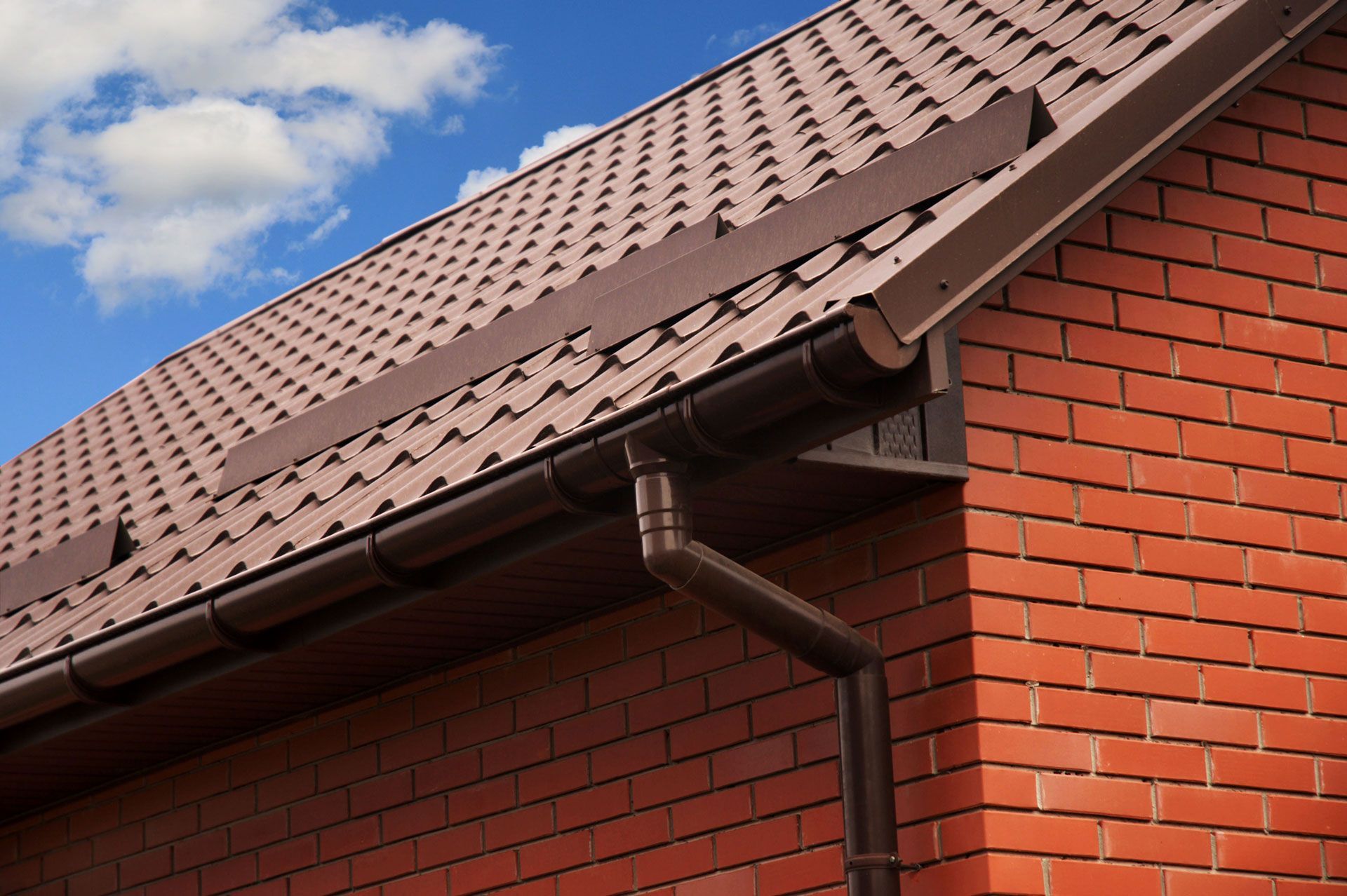 A brick building with a brown roof and a black gutter.