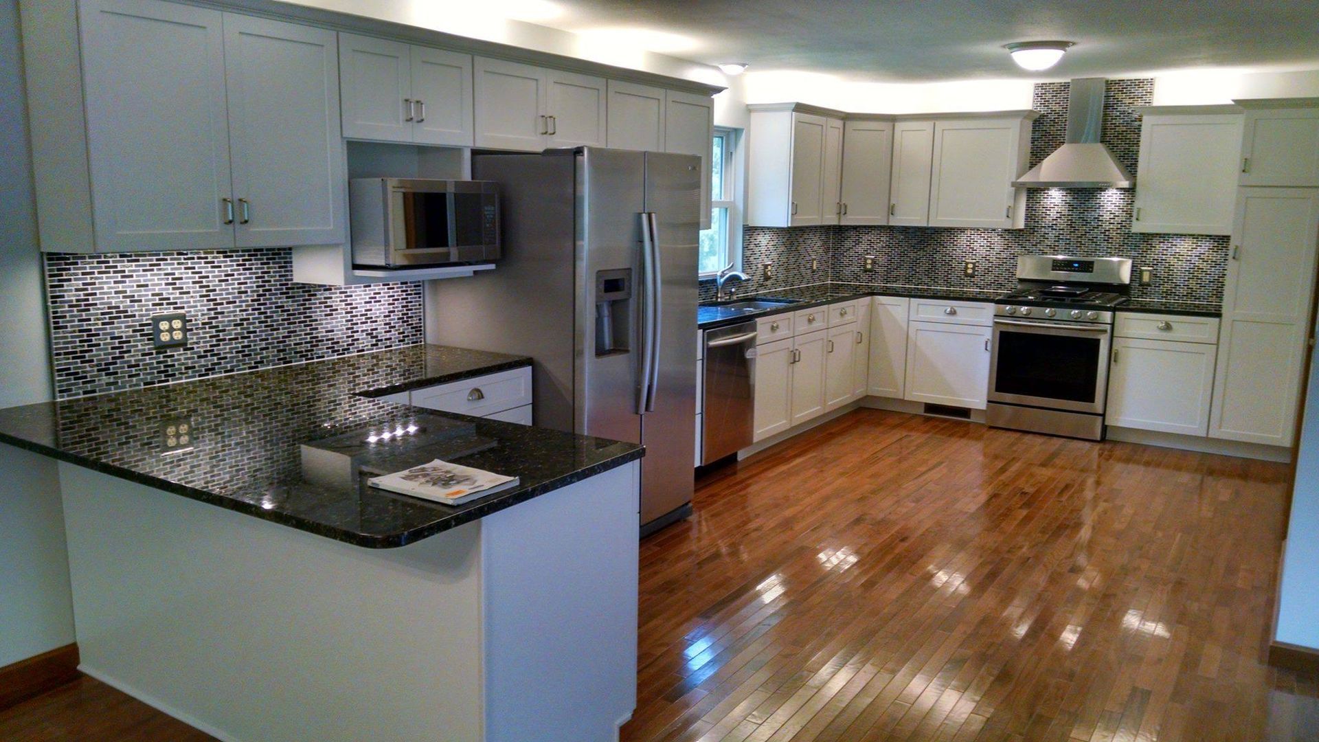A kitchen with white cabinets , stainless steel appliances , granite counter tops and hardwood floors.