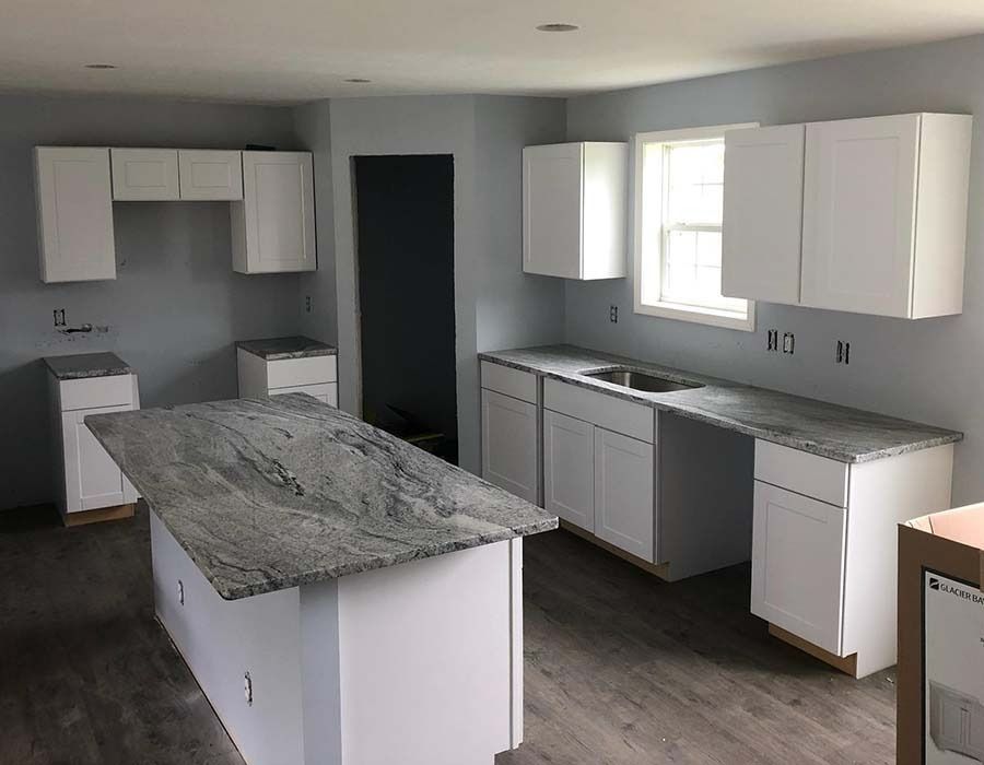 A kitchen with white cabinets , granite counter tops , and a large island.