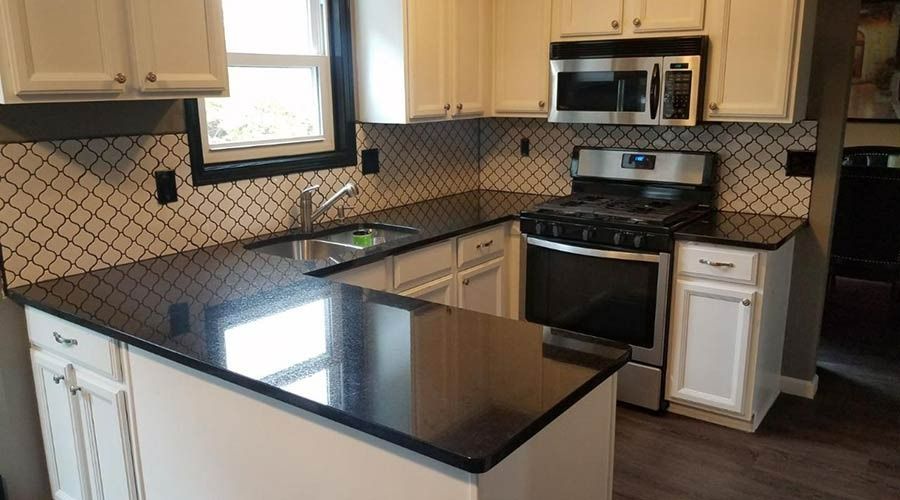 A kitchen with white cabinets , black counter tops , a stove , microwave and sink.