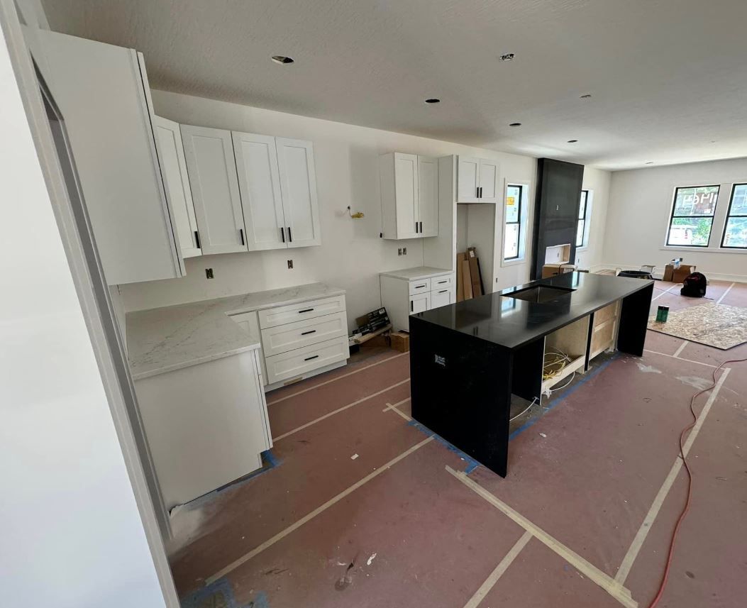 A kitchen under construction with white cabinets and a black island