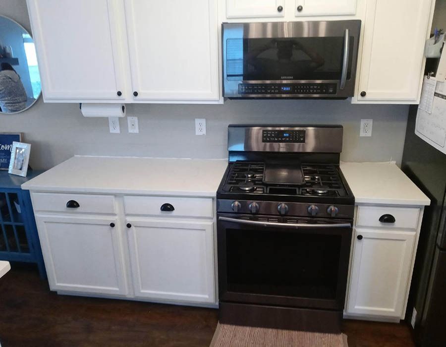 A kitchen with white cabinets , a stove and a microwave.