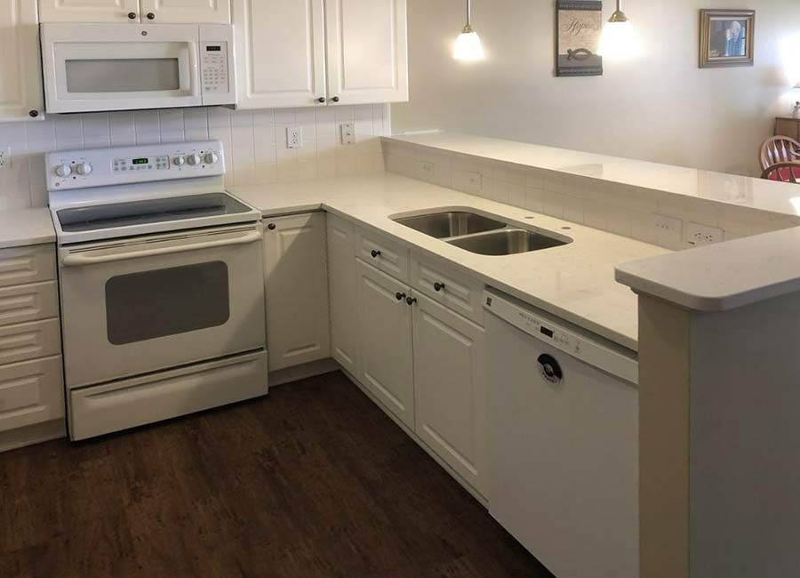A kitchen with white cabinets , a stove , a microwave , and a sink.