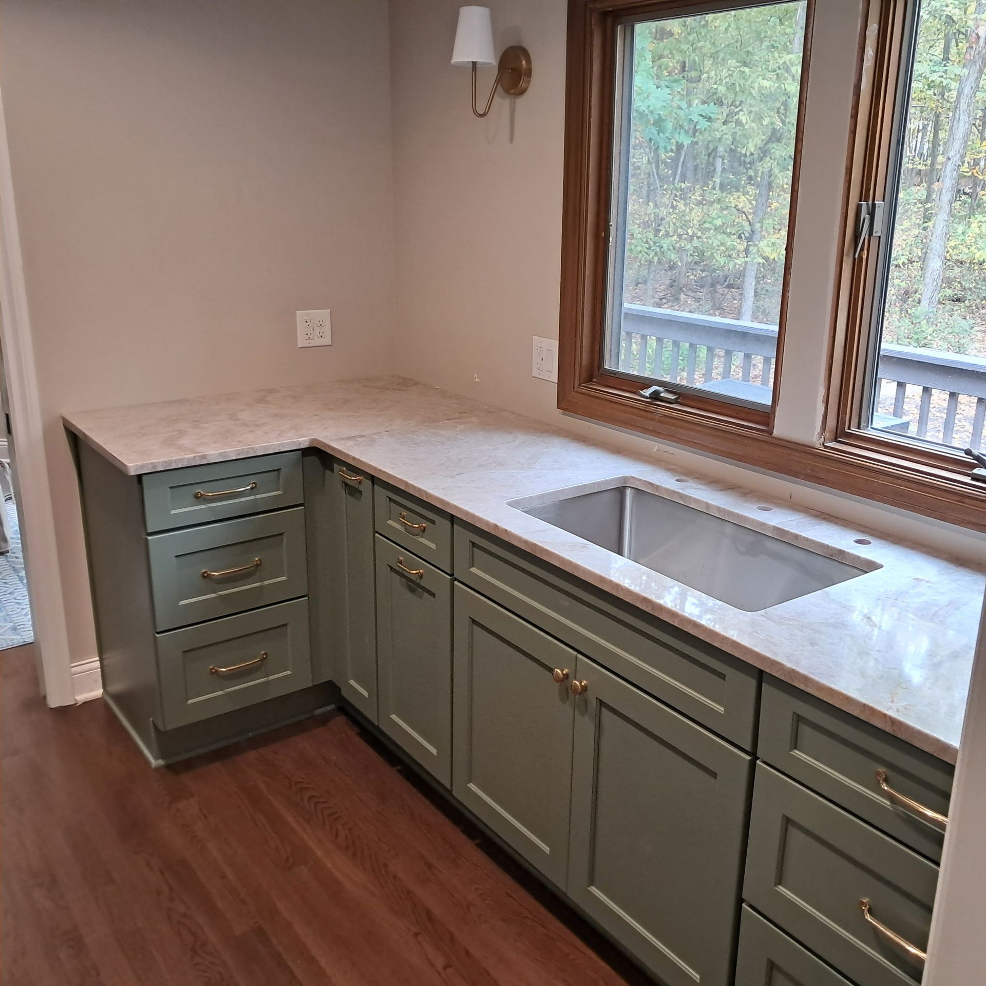 Green kitchen cabinets with light countertops and a sink by a window.