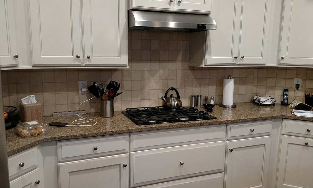 A kitchen with white cabinets , granite counter tops , a stove and a hood.