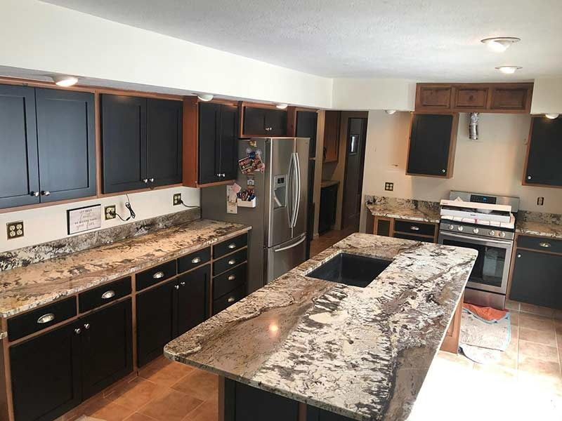 A kitchen with granite counter tops , black cabinets and stainless steel appliances.